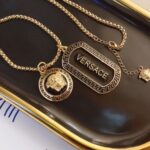 سلسلة ذهبية بتصميم مستوحى من Versace مع تعليقة ميدوسا ونقشة يونانية.